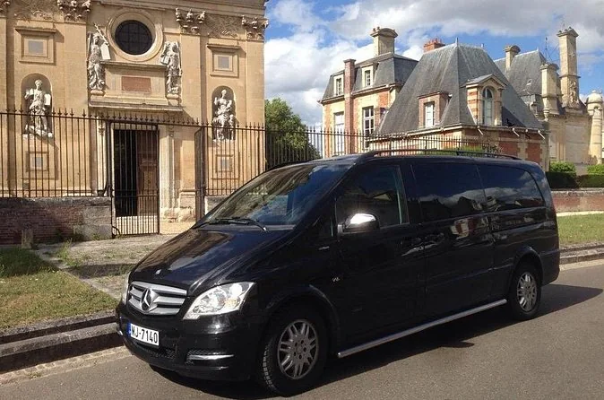 A black Mercedes minivan parked on a street in front of stone buildings