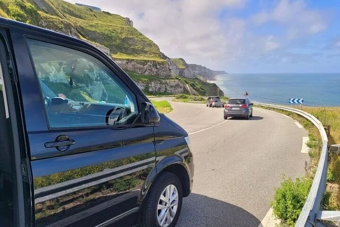A black van on a winding coast road with green cliffs and the sea beside it