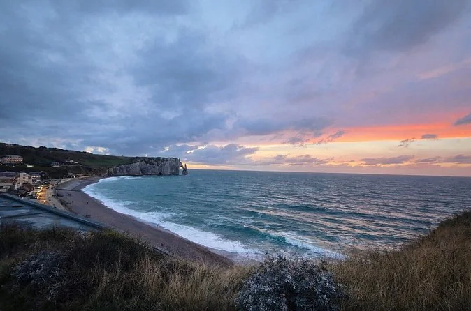 Die Bucht von Étretat von oben bei Sonnenuntergang, mit rosa Himmel über dem Meer und dem Bogen des Strands