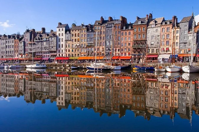 Honfleur's tall harbour houses reflected in calm water under a blue sky