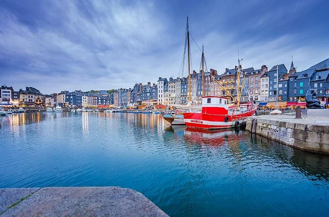 A red boat in Honfleur harbour with tall slate-fronted houses along the quay