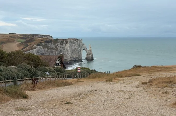 Un sentier herbeux en haut de la falaise menant vers la falaise d'Aval et son arche au-dessus d'une mer turquoise